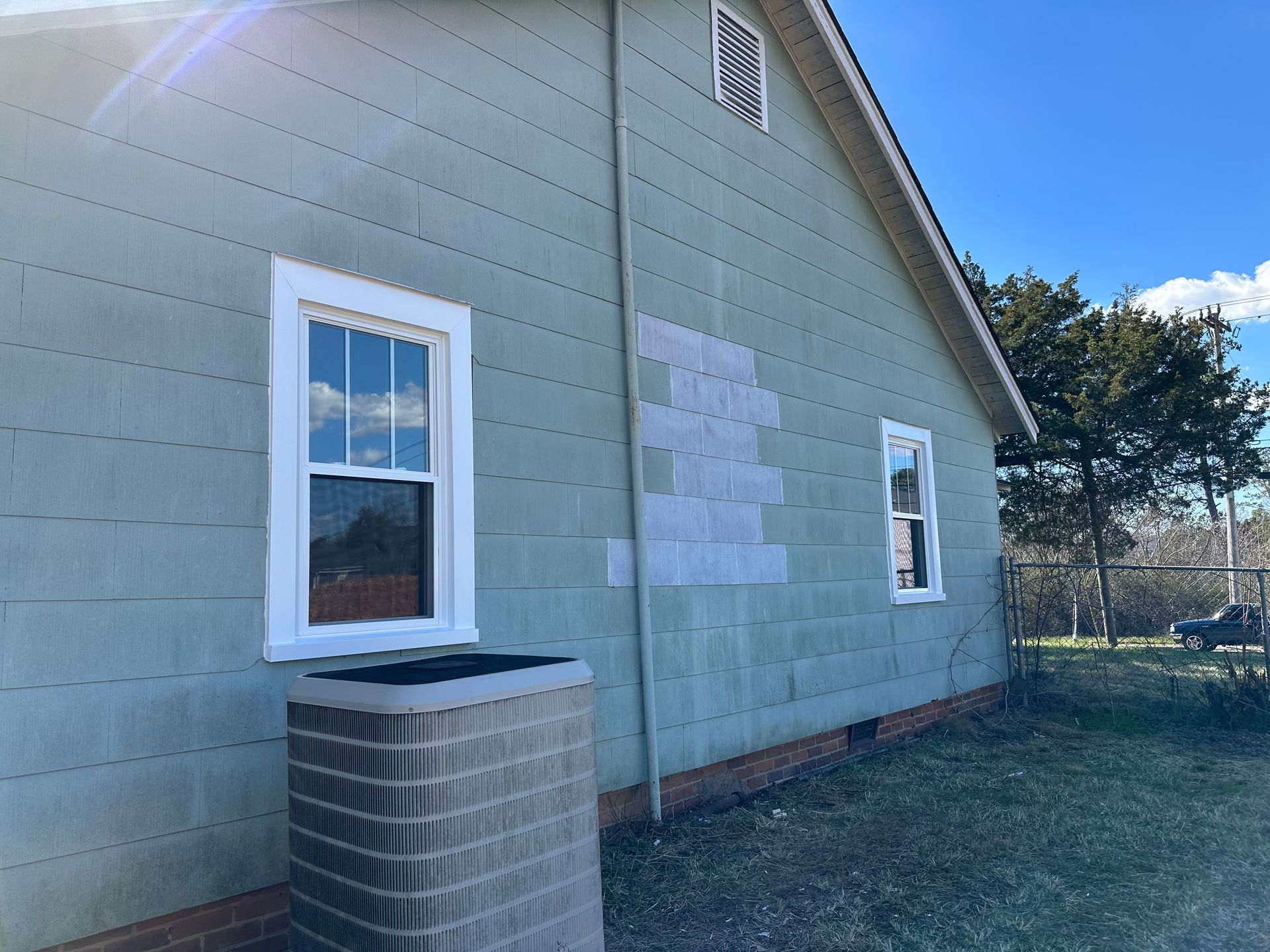 The side of a house with two windows and an air conditioner.
