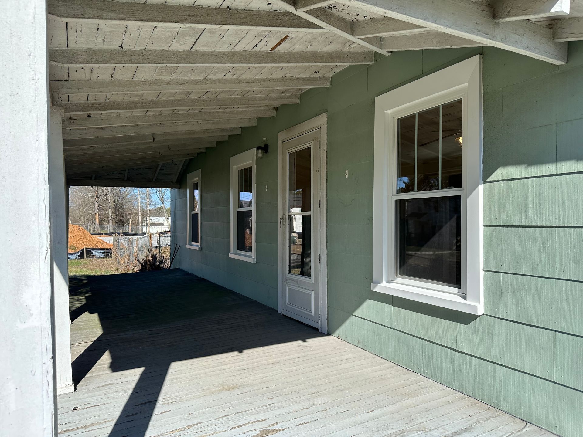 A green house with a porch and a white roof.