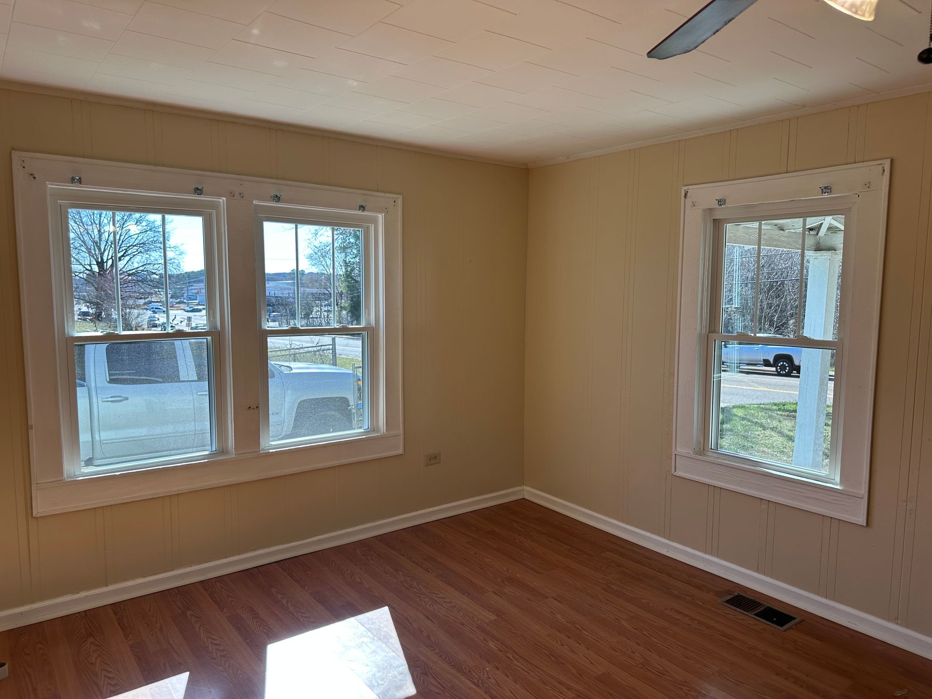 An empty room with two windows and a ceiling fan.