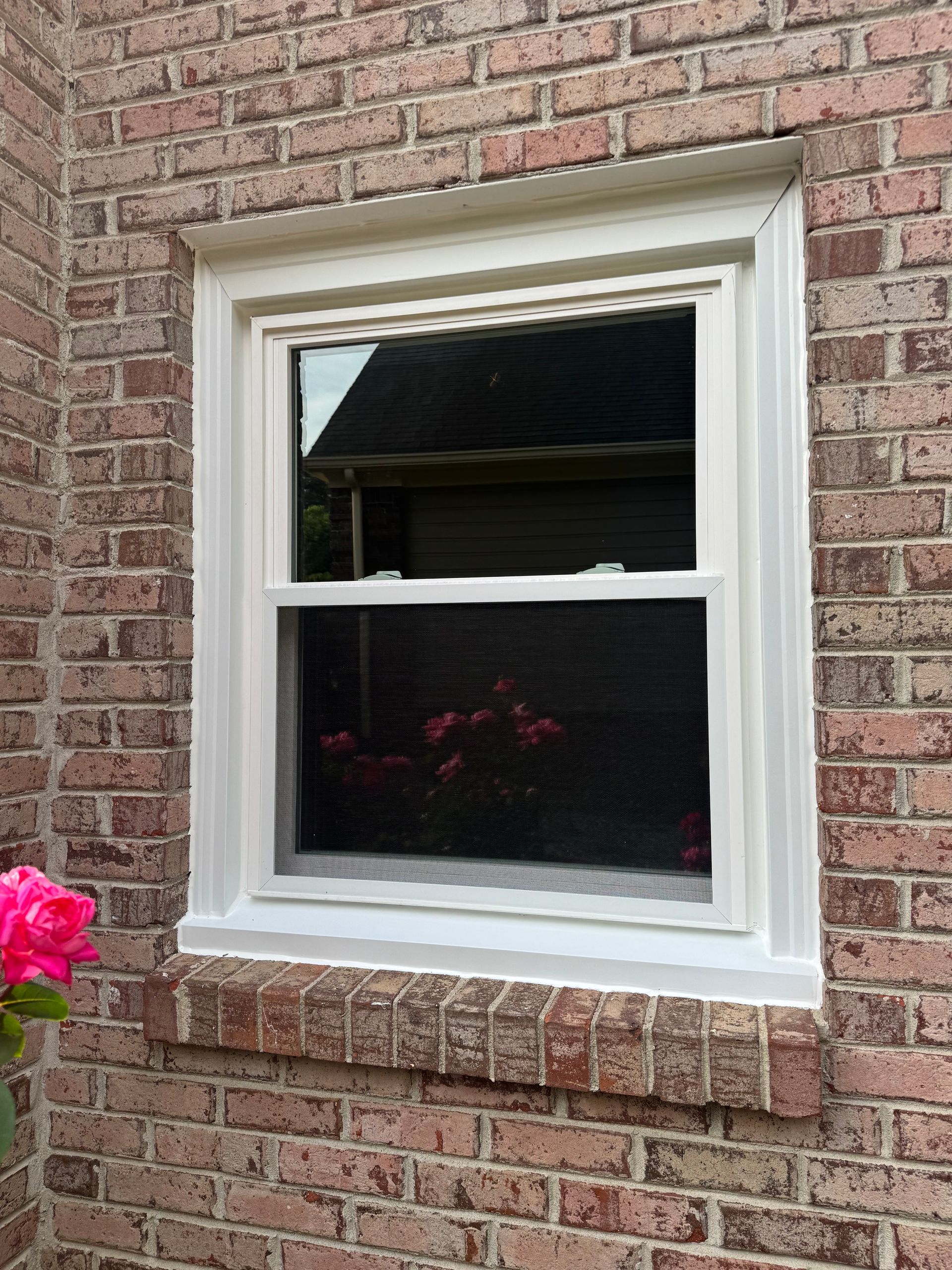 A white window is on the side of a brick building.