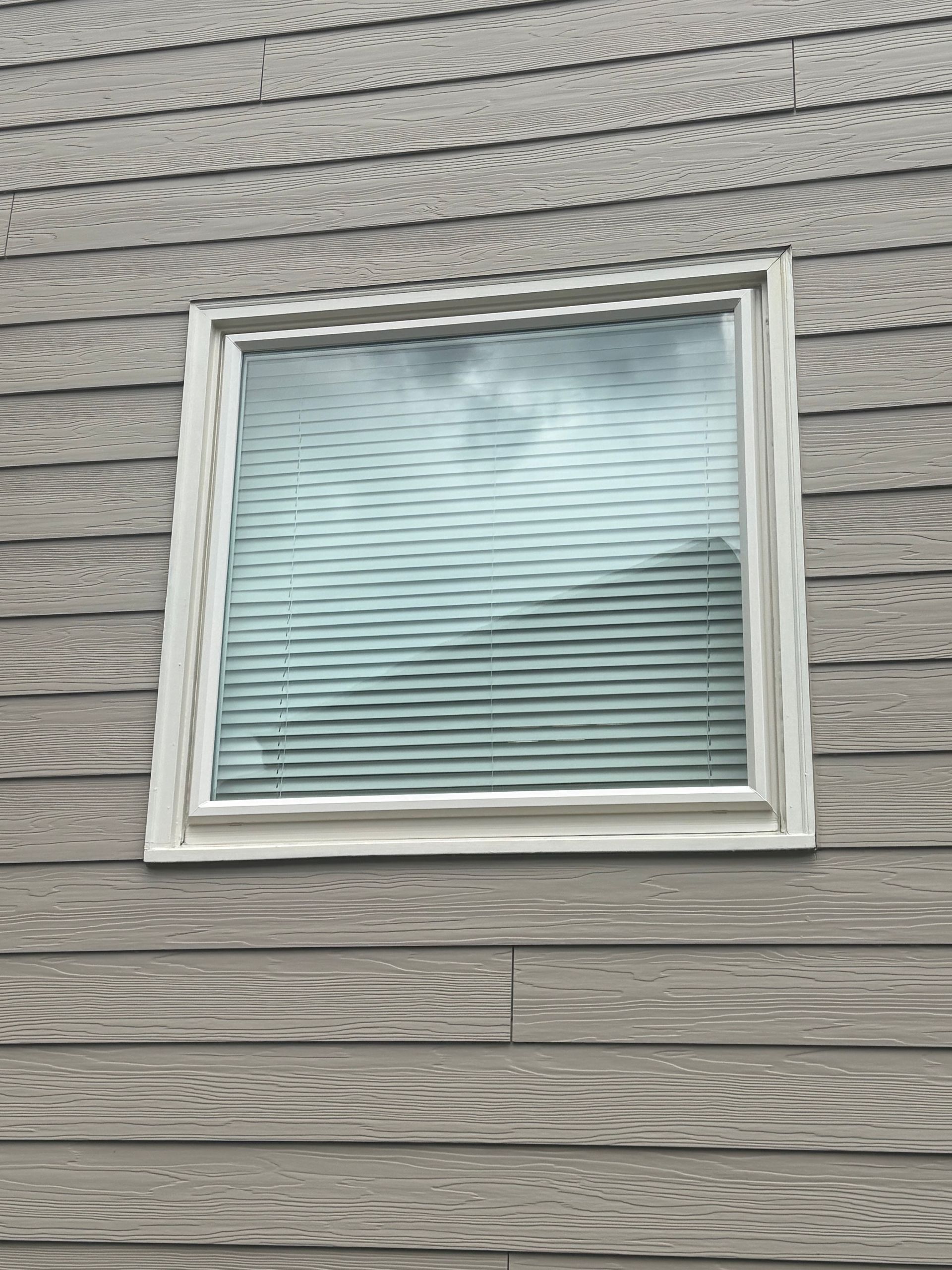 A square window on the side of a house with blinds.