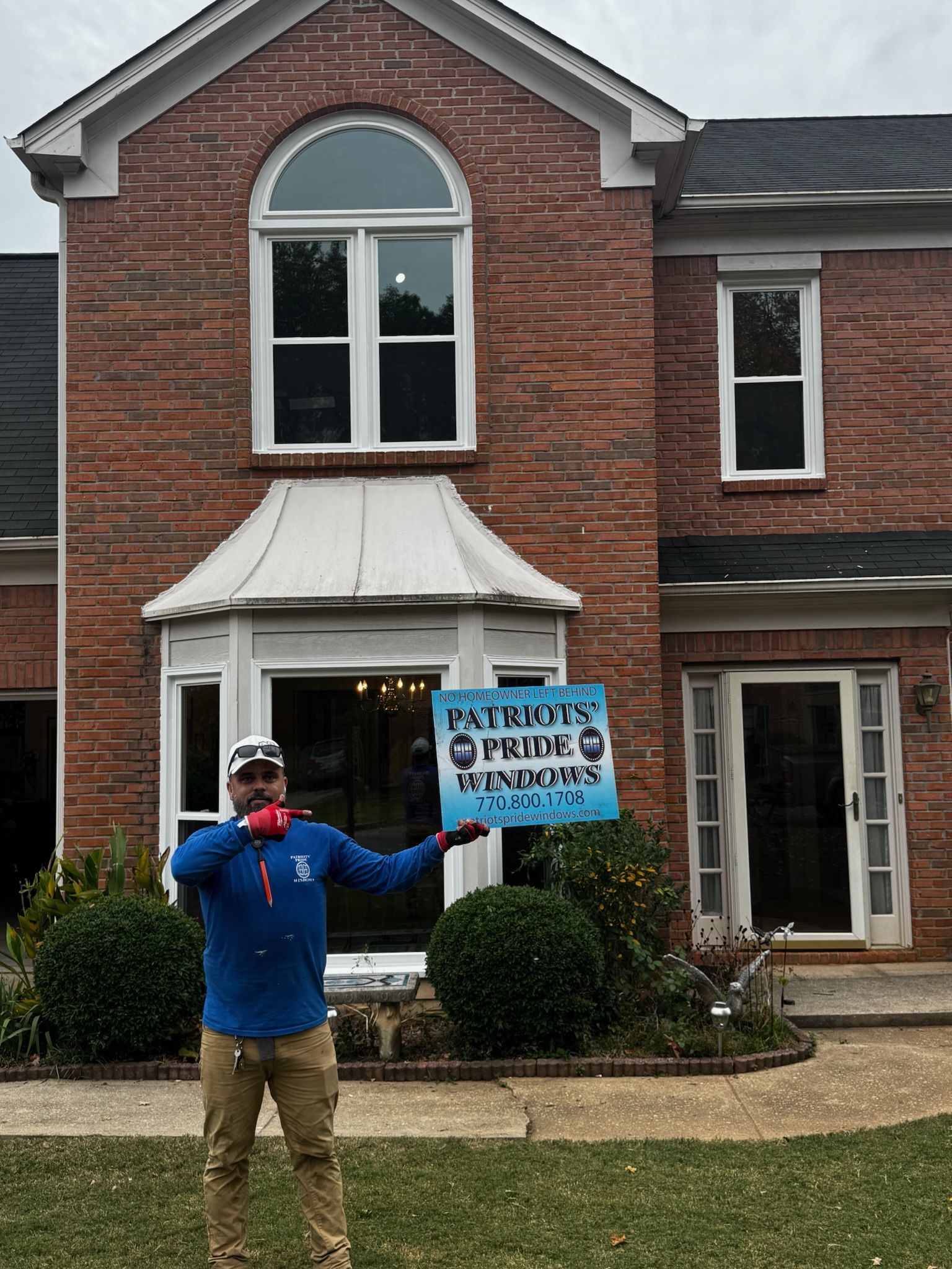 A man is holding a sign in front of a large brick house.