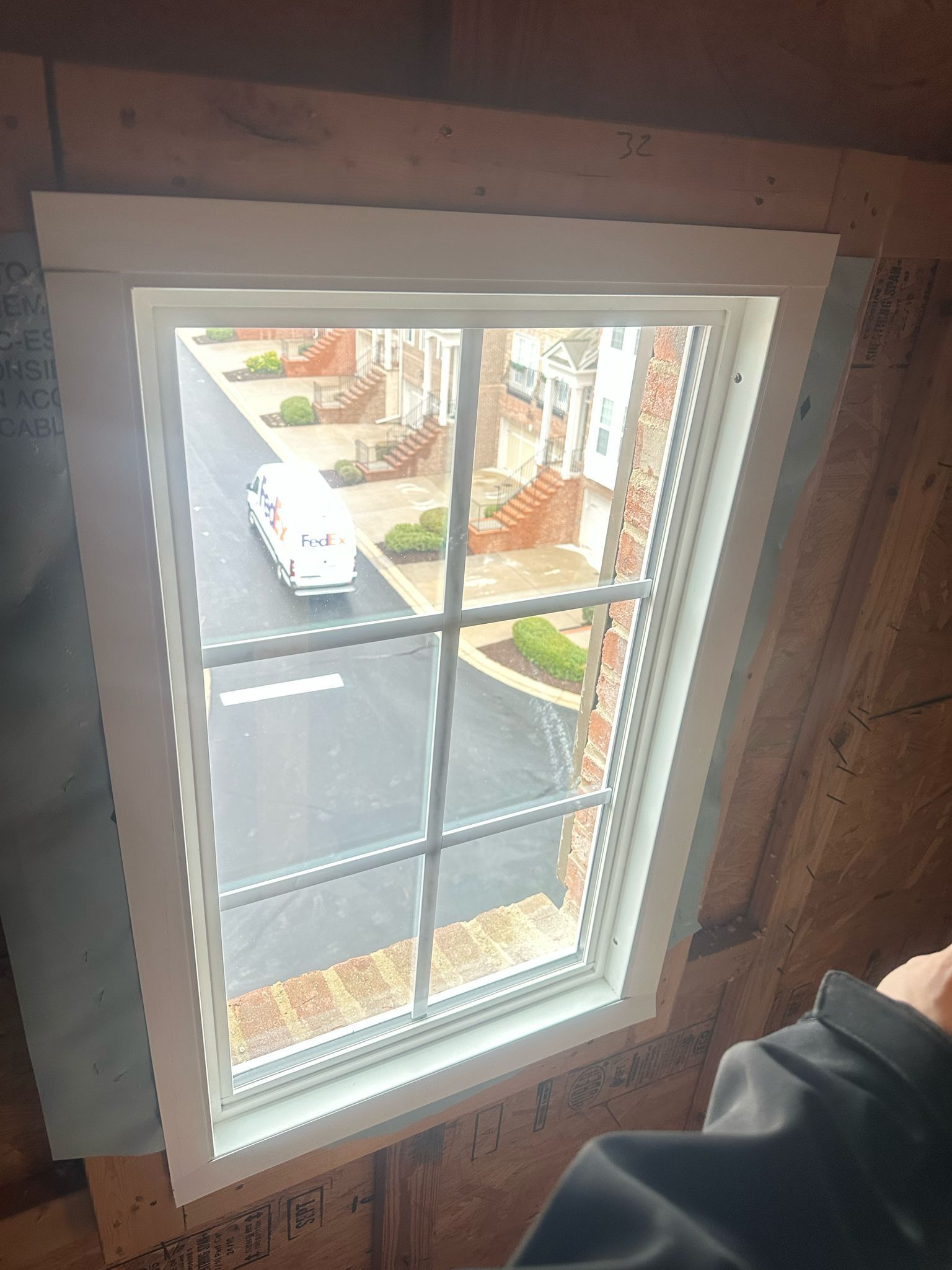 A person is standing in front of a window with a view of a street.