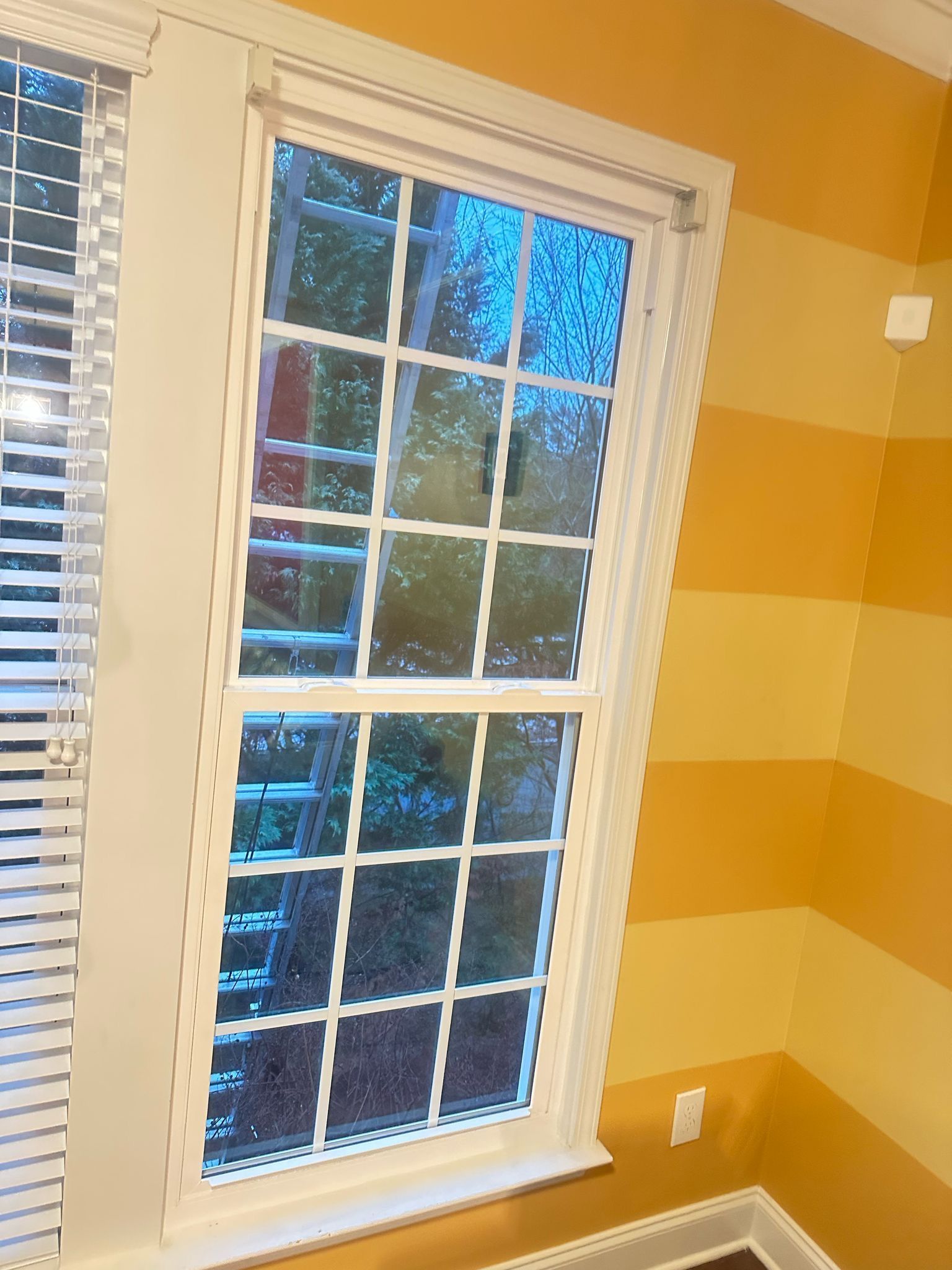 A window with blinds in a room with yellow stripped walls.