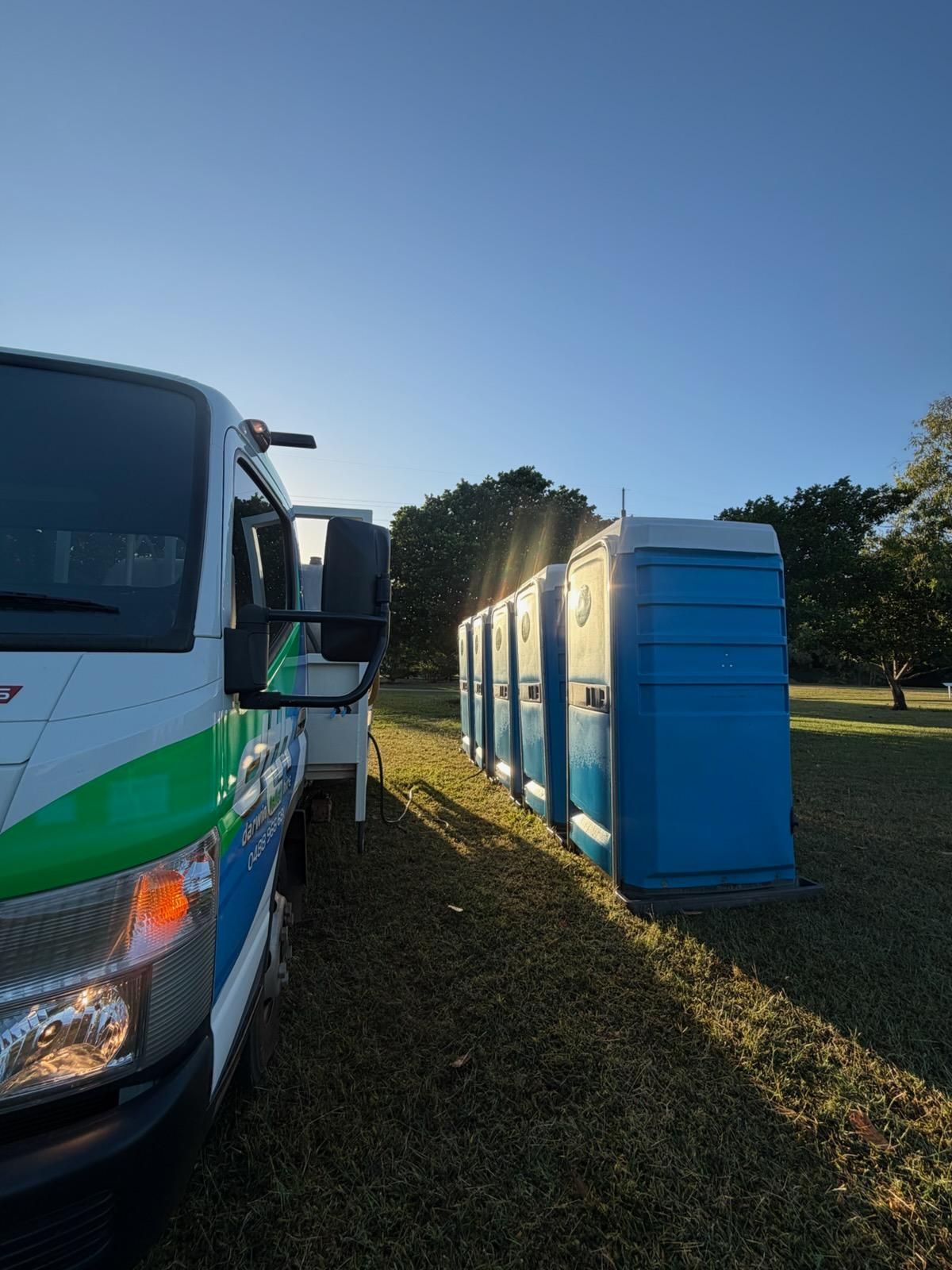 White Truck Beside Blue Portable Toilets on a Grassy Field — Darwin Toilet Hire in Rosebery, NT