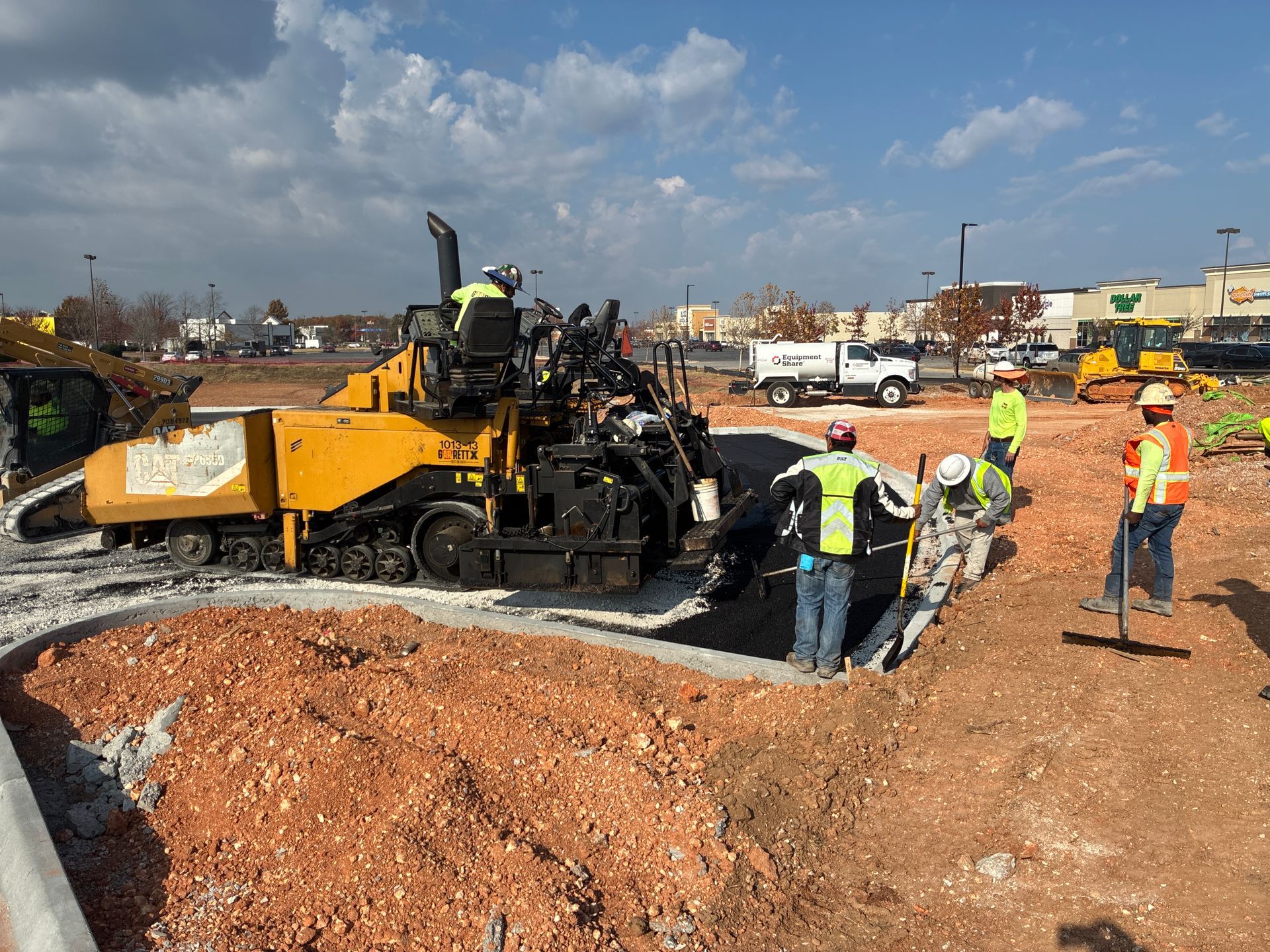 Yellow asphalt paving machine laying road surface; workers nearby. Outdoors, sunny day.