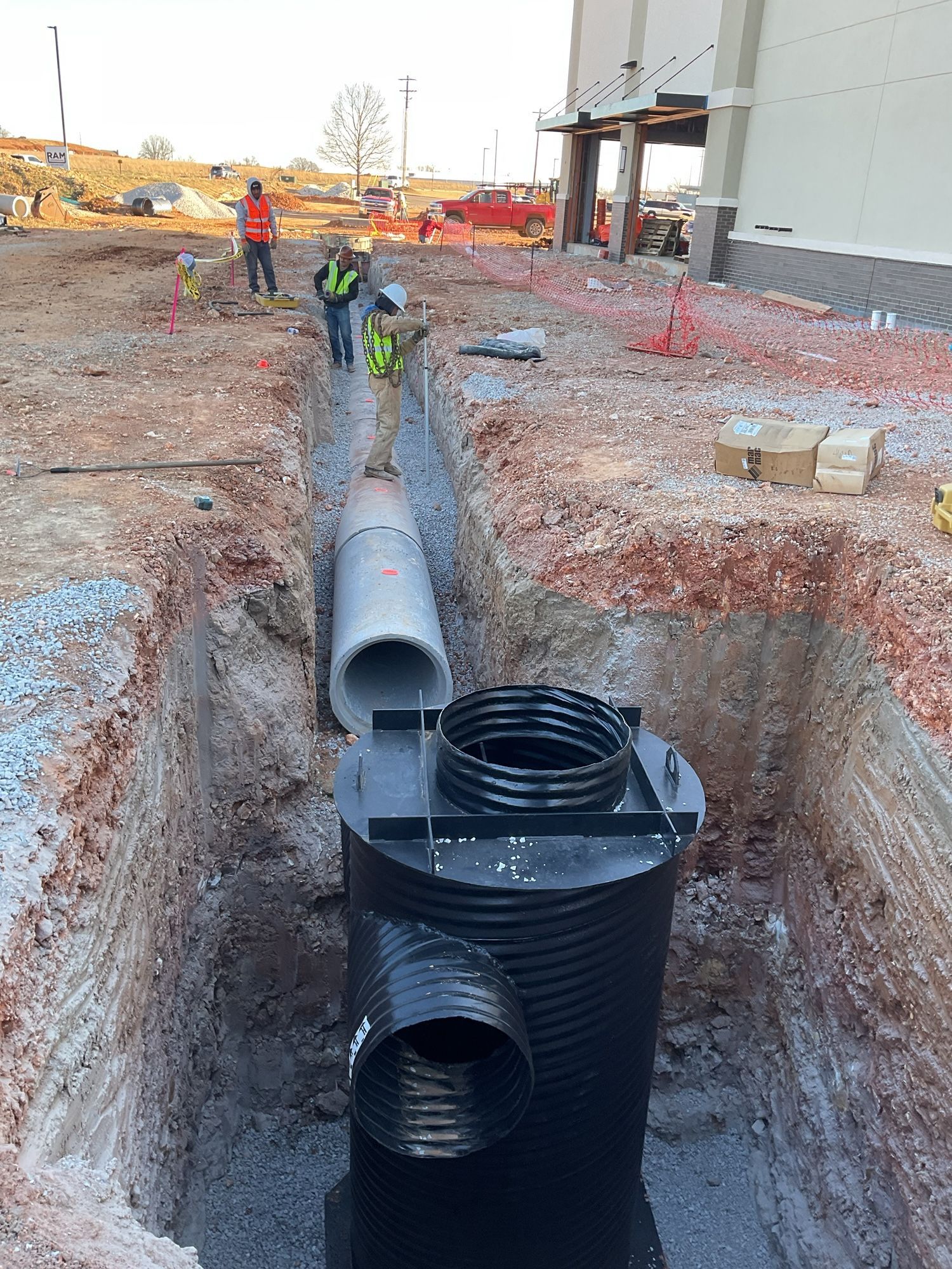 Construction workers installing a drainage system in an excavated trench near a building.
