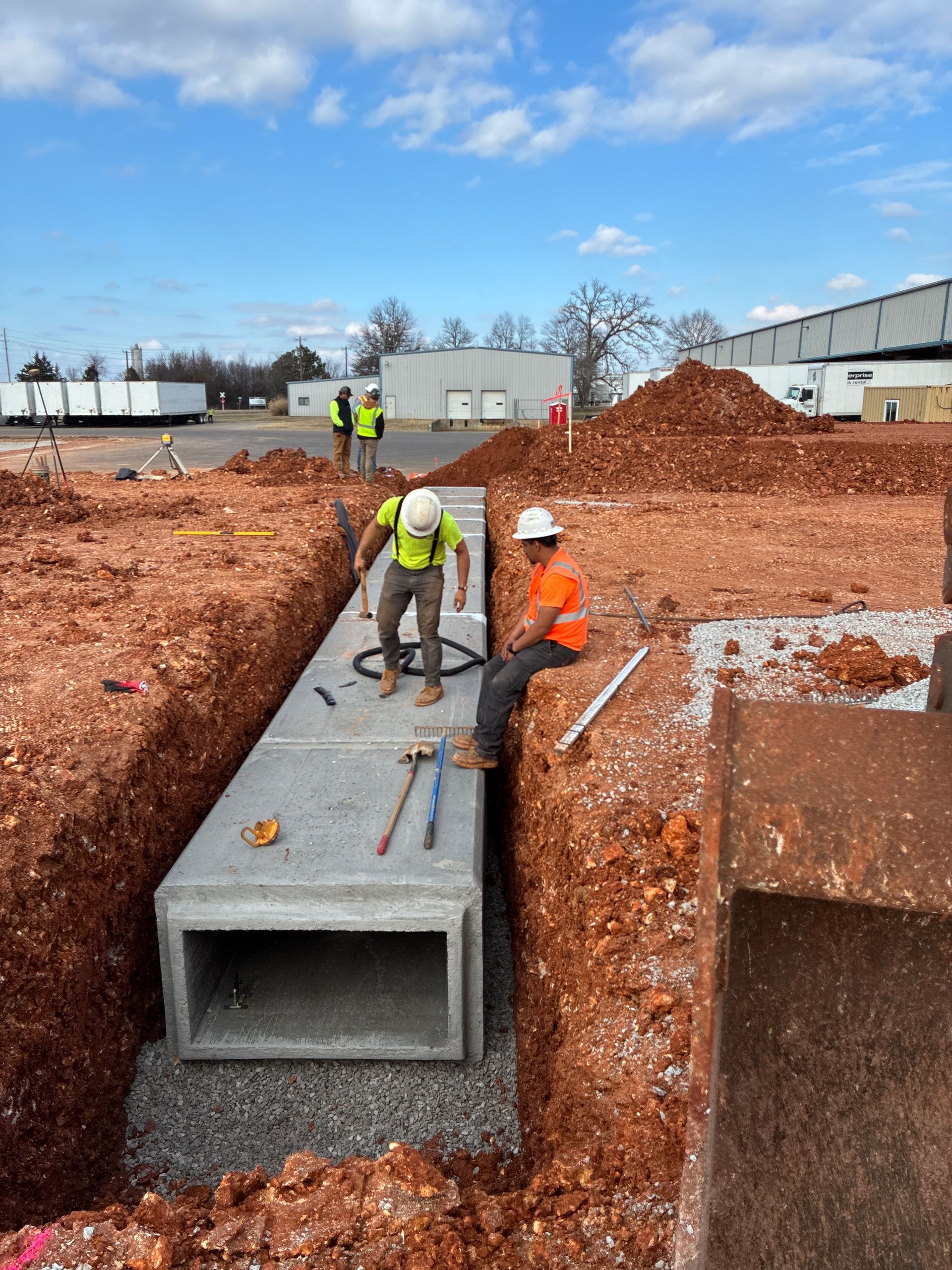 Construction workers installing a concrete drainage culvert in an excavated trench outdoors.