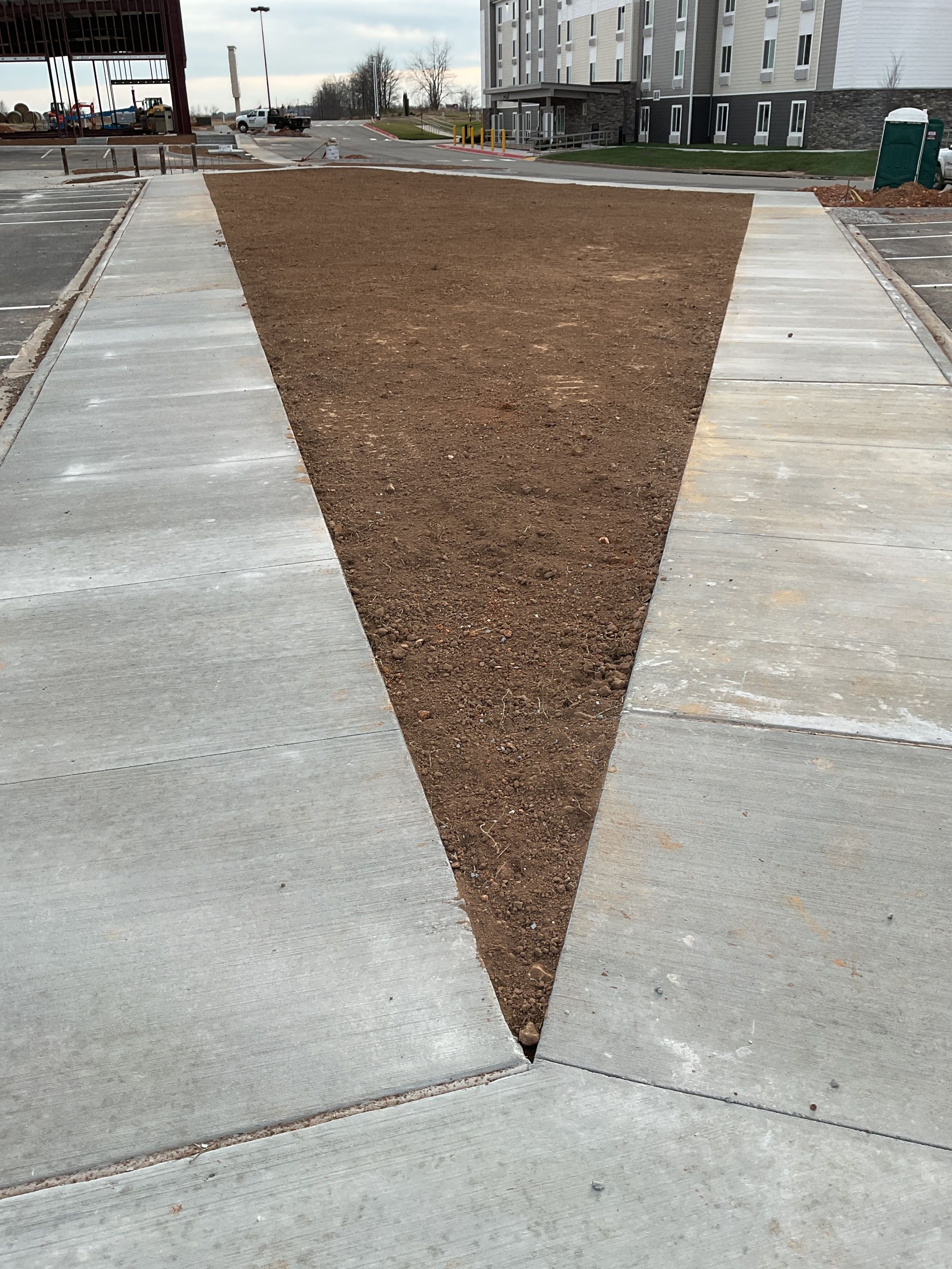 Gravel triangle path between concrete sections. Buildings and road in the background.