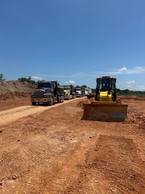 Construction site: Bulldozer and trucks on a dirt road under a blue sky.