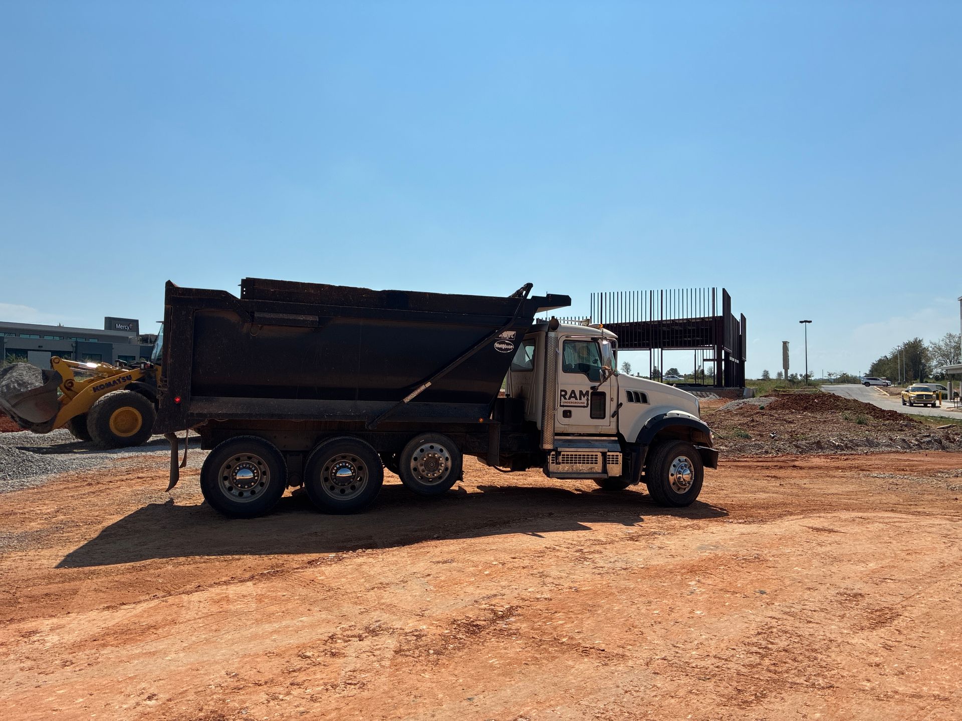 Dump truck on a construction site with a yellow loader and steel framework. Blue sky.