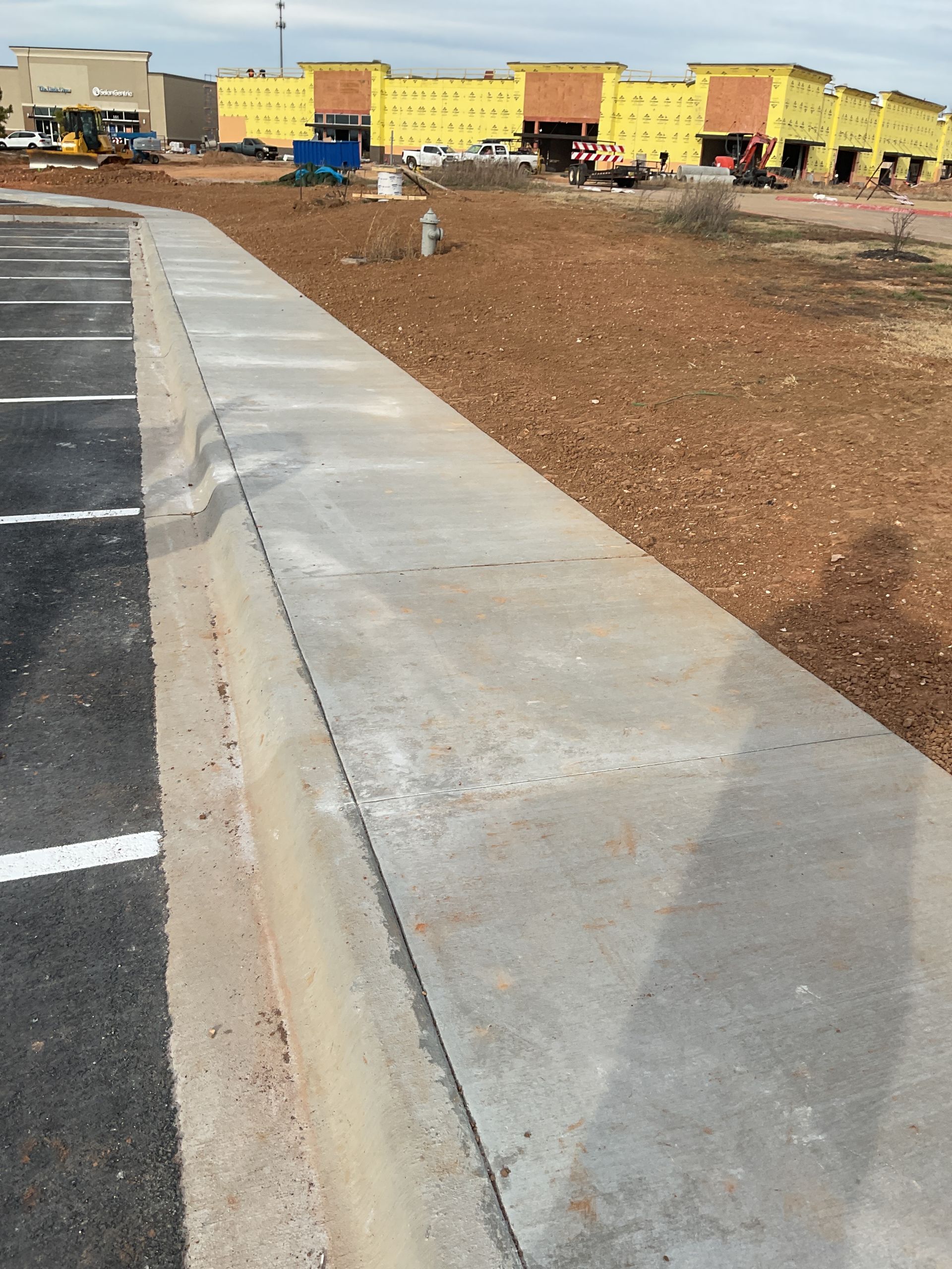 Concrete curb next to asphalt parking lot with construction site in the background.