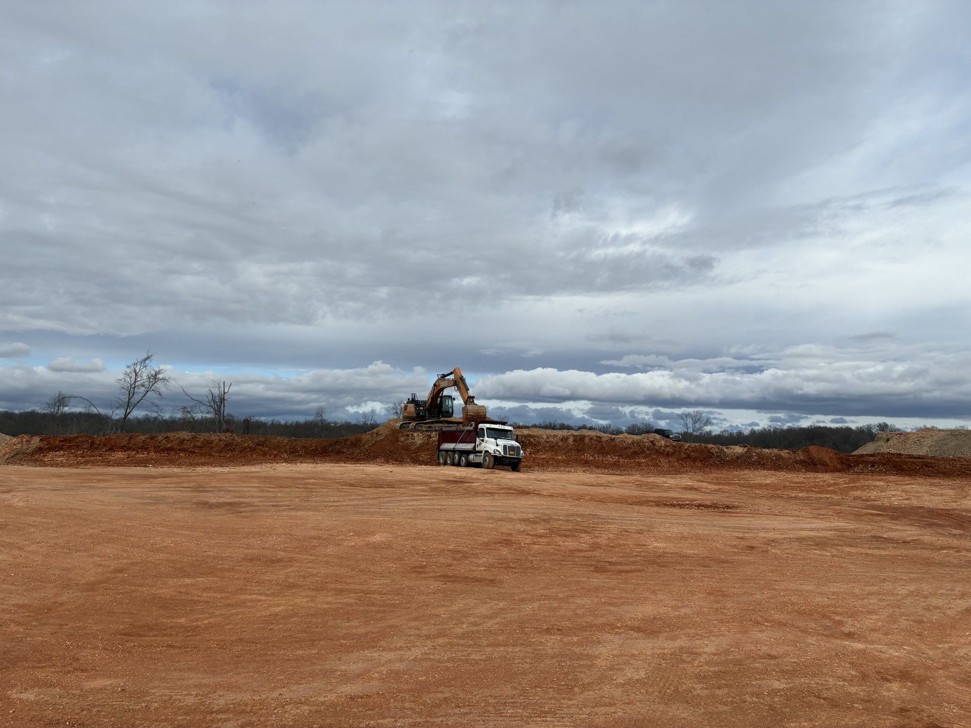 Heavy machinery loading a truck with wood chips under a cloudy sky.