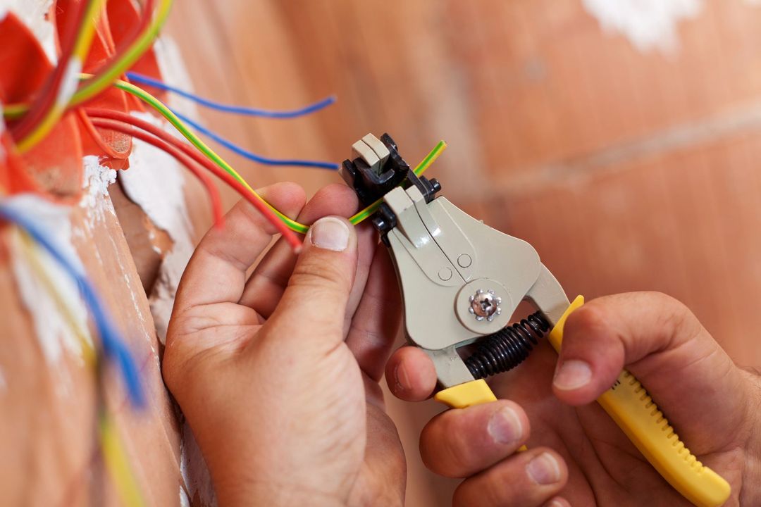Persona che rimuove l'isolamento da un filo elettrico verde con uno spelafili vicino a una scatola elettrica.