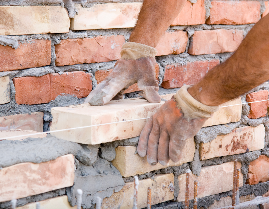 Mani di un muratore che posizionano un mattone su un muro parzialmente costruito con la malta.