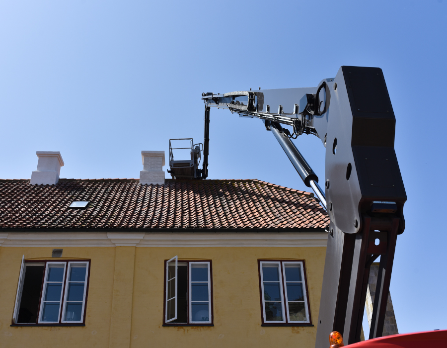 Gru al lavoro sul tetto di un edificio giallo con finestre aperte; cielo azzurro sullo sfondo.