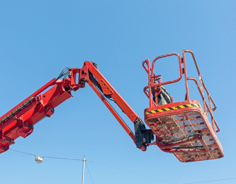 Braccio di sollevamento e cesto di una piattaforma aerea rossa contro un cielo azzurro terso.
