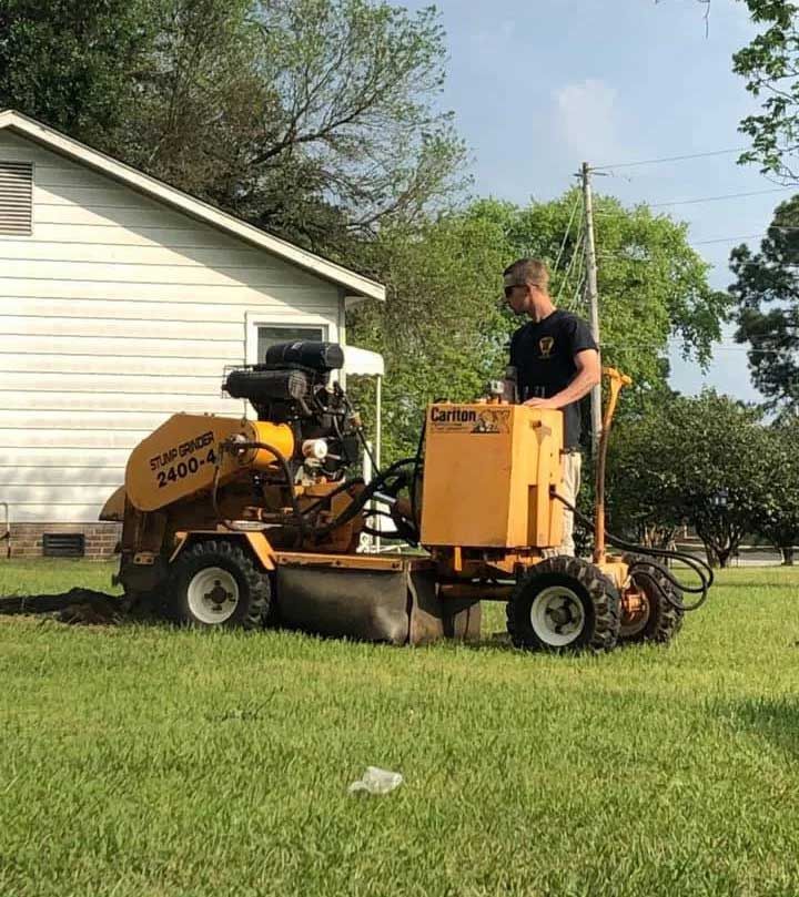 A man is driving a stump grinder in a yard.