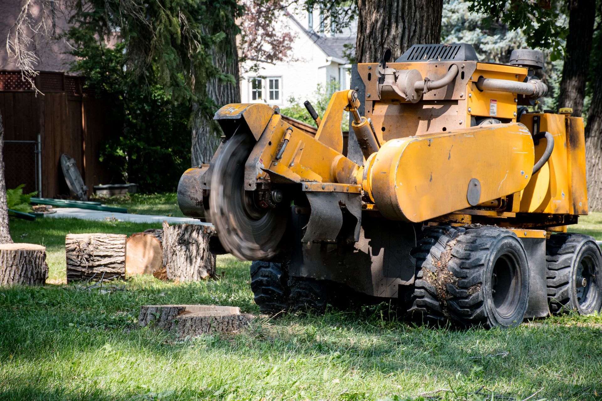 A yellow stump grinder is sitting in the grass next to a tree stump.