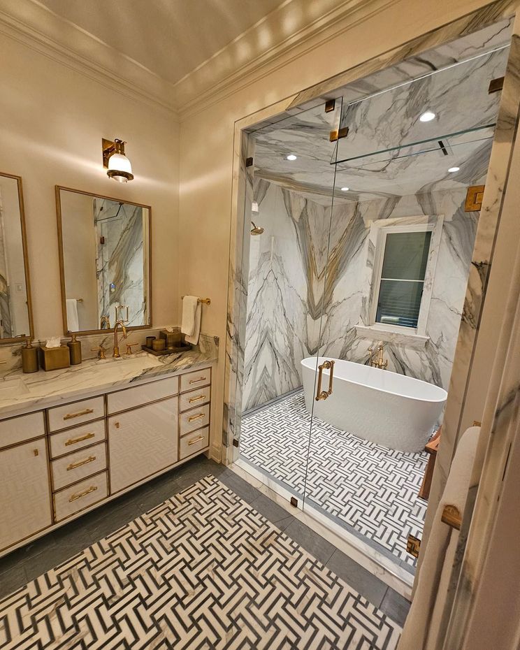 Luxurious bathroom with marble shower, freestanding tub, gold accents, and geometric floor tile.