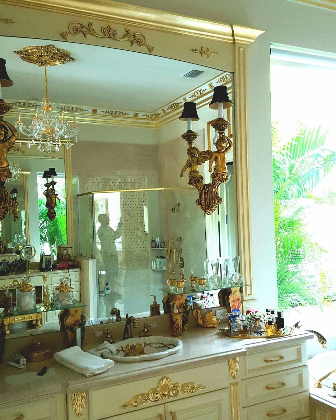 Ornate bathroom with gold trim, large mirror, chandelier, and vanity.