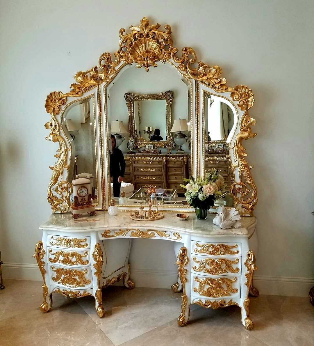 Ornate white vanity with gold accents and a large, tri-paneled mirror.