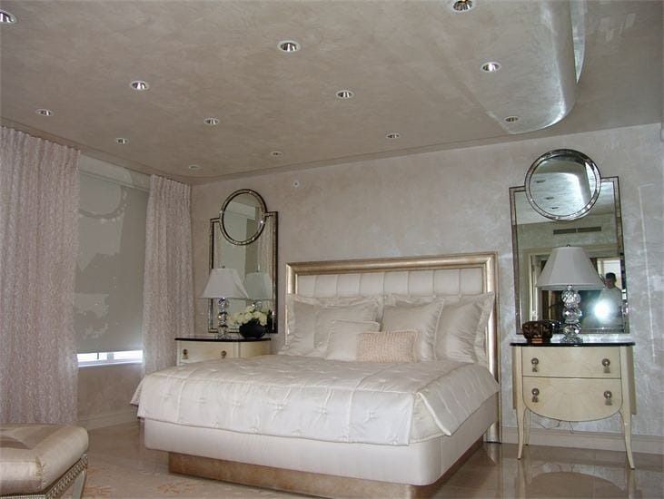 Elegant white bedroom with a large bed, two nightstands, and matching mirrors.