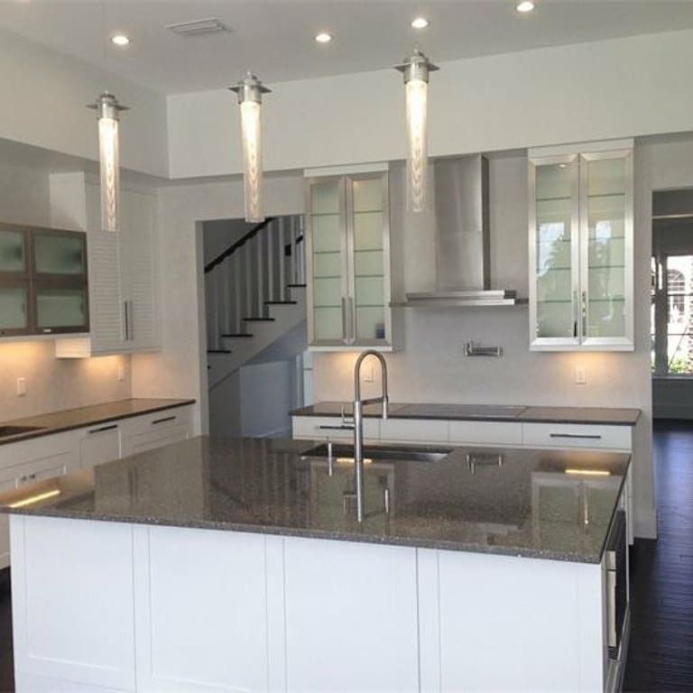 Modern white kitchen with island, stainless steel appliances, and pendant lights.