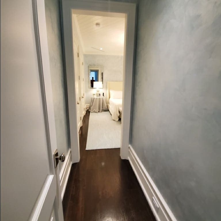 Hallway leads to a light-filled bedroom; walls are blue, door frames white, hardwood floor, and a rug on the floor.