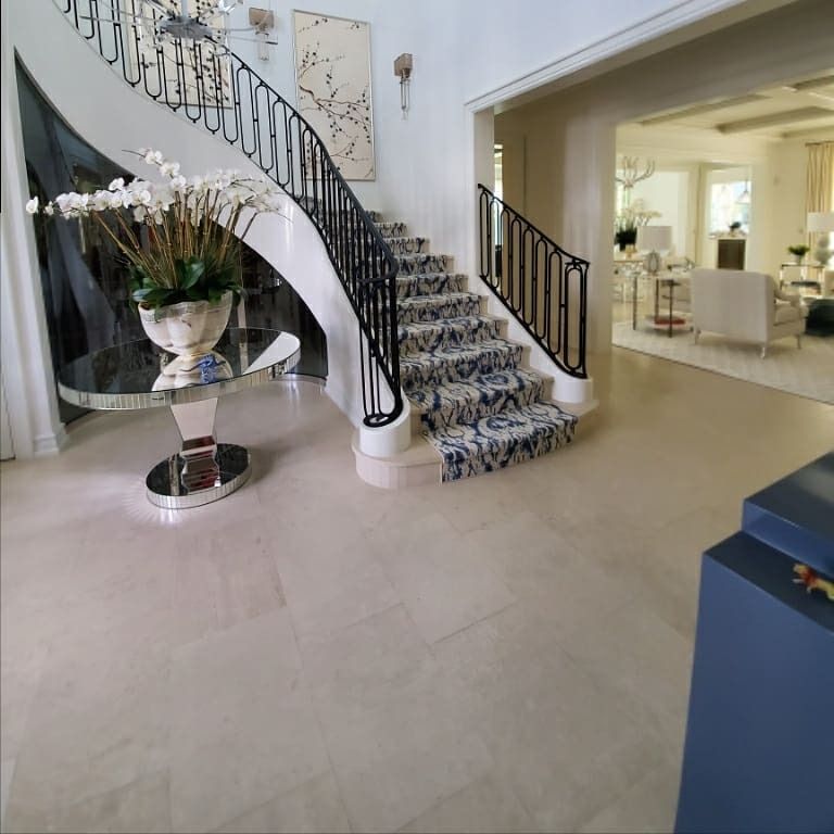 Elegant entryway with staircase and patterned runner, light-colored floors and walls, flowers in a vase.
