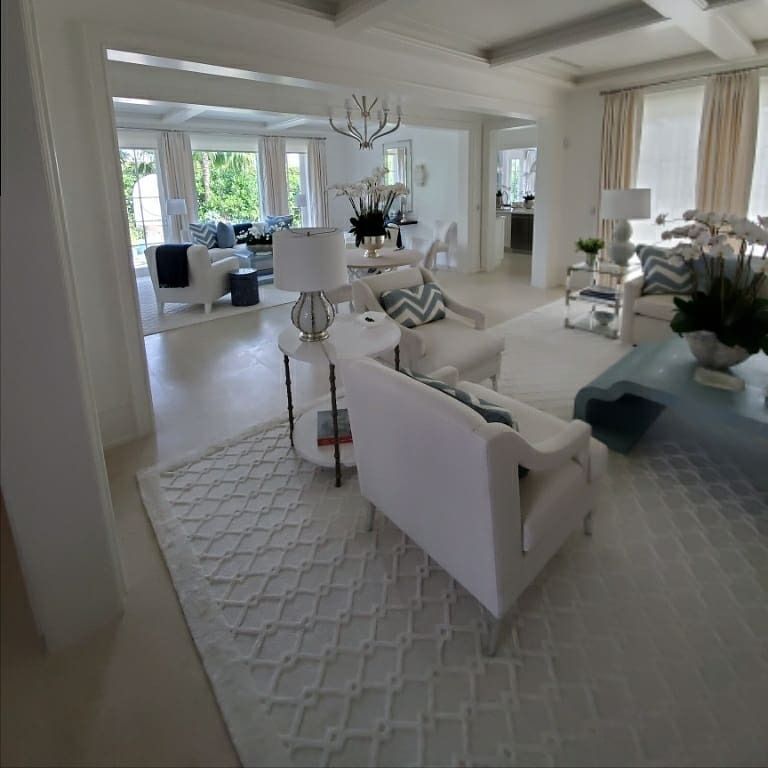Spacious white living room with light blue accents, various seating, rug, and chandelier.