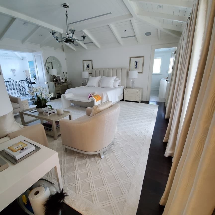 Elegant white bedroom with cream accents, a bed, seating area, and a dark floor.