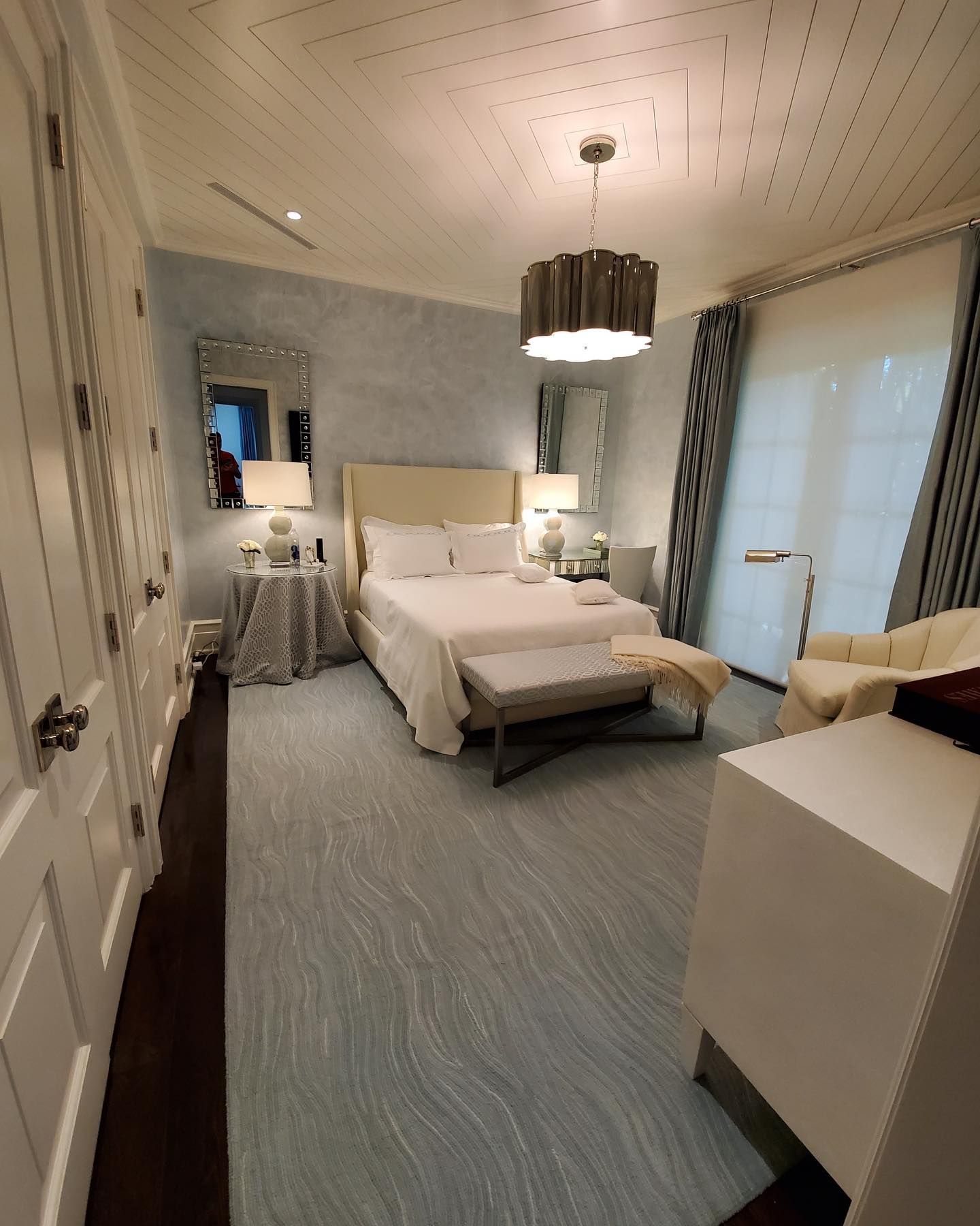 Bedroom with light blue walls, white furniture, and a large patterned rug.