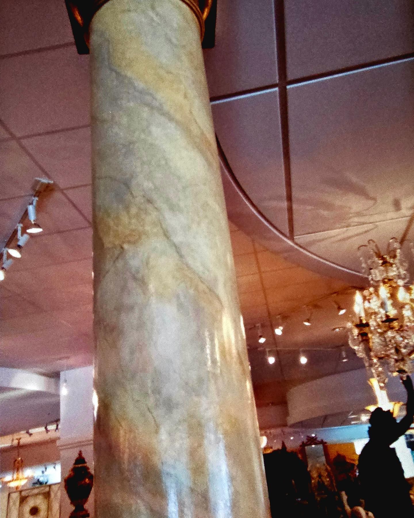 Marble column in a room with lighting and a silhouetted figure reaching towards a chandelier.