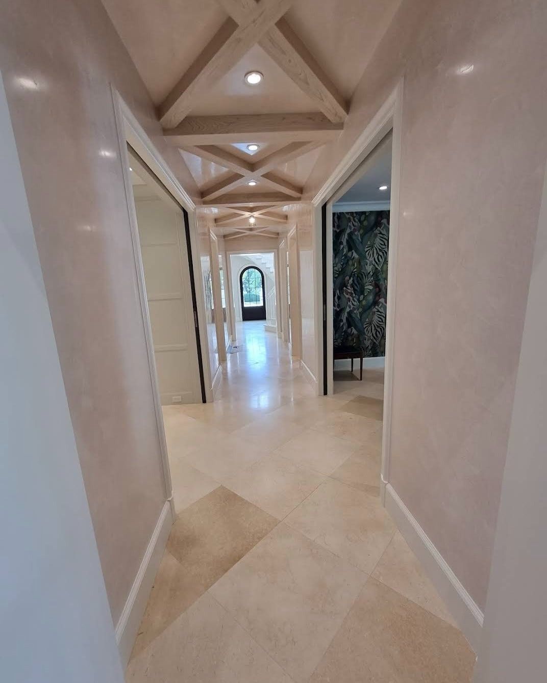 Long hallway with beige tiled floor, light pink walls, and decorative wood ceiling beams.