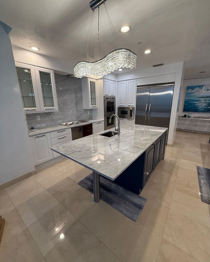 Modern kitchen with marble island, stainless steel appliances, and crystal chandelier.