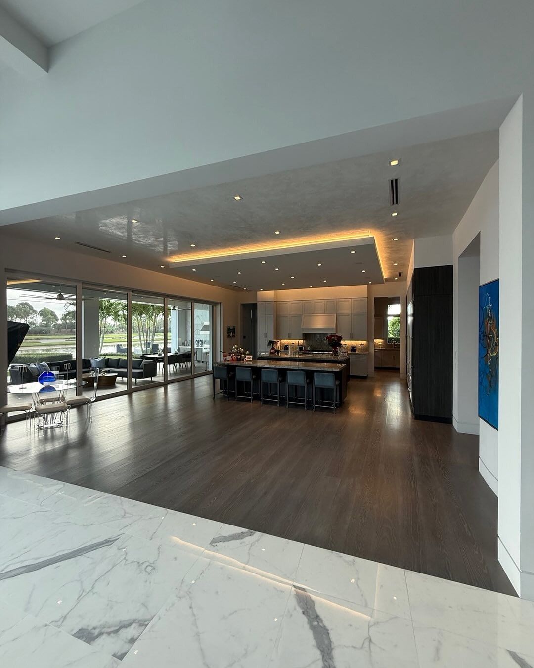 Spacious modern kitchen with island, dark wood floors, and large windows overlooking a green space.