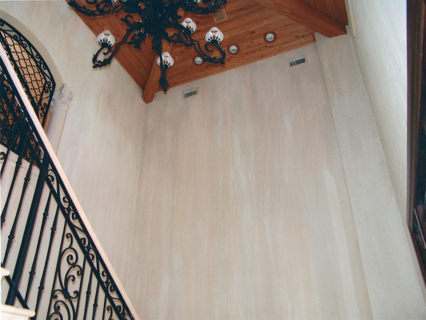 Staircase with wrought iron railing and chandelier hanging from wood-paneled ceiling.