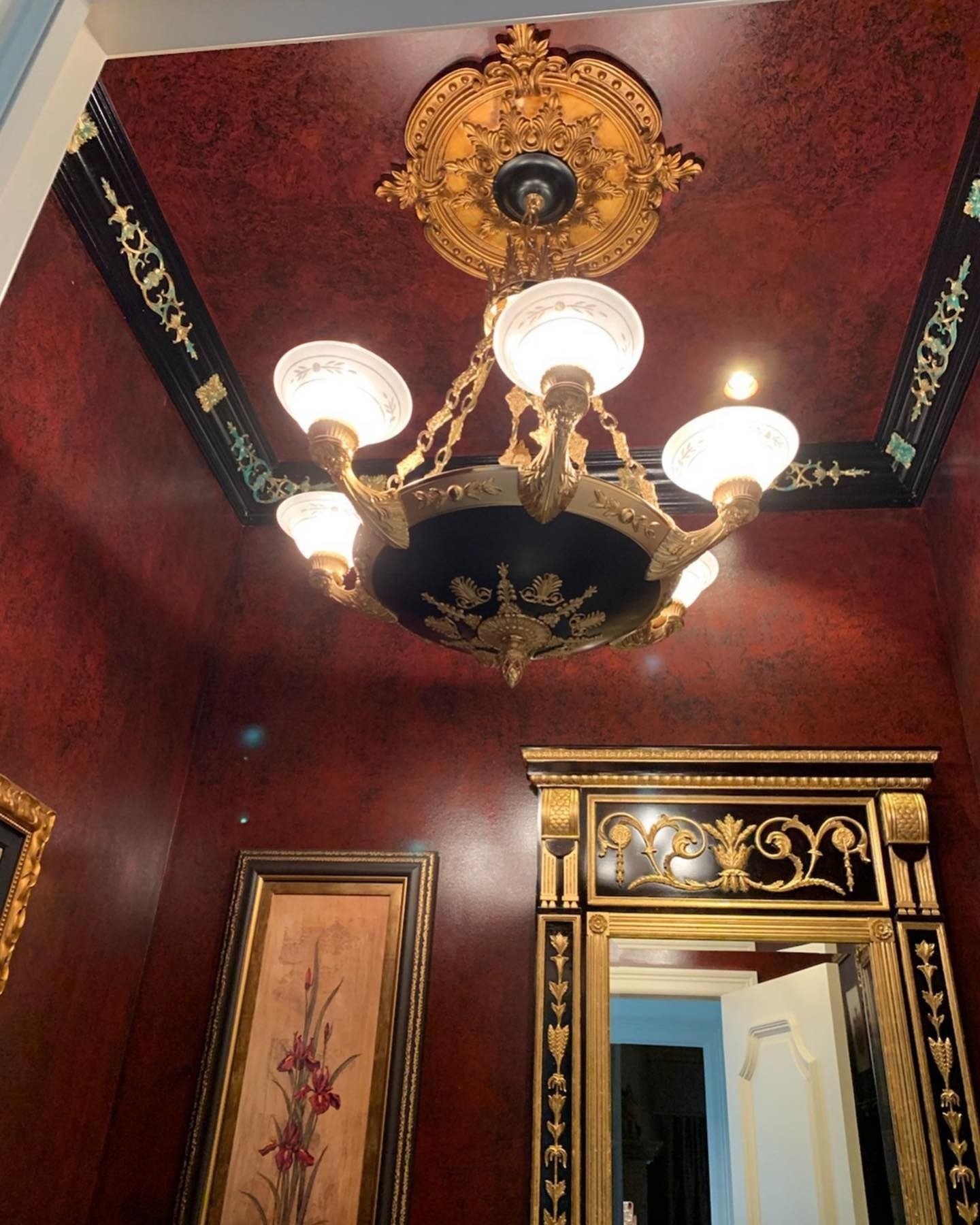 Ornate room with chandelier, red walls, black and gold trim, and a mirror.