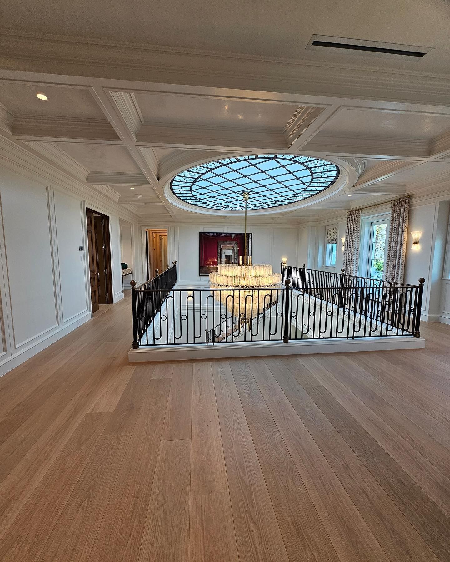 Spacious room with hardwood floors, staircase with black railing, and an overhead circular skylight.