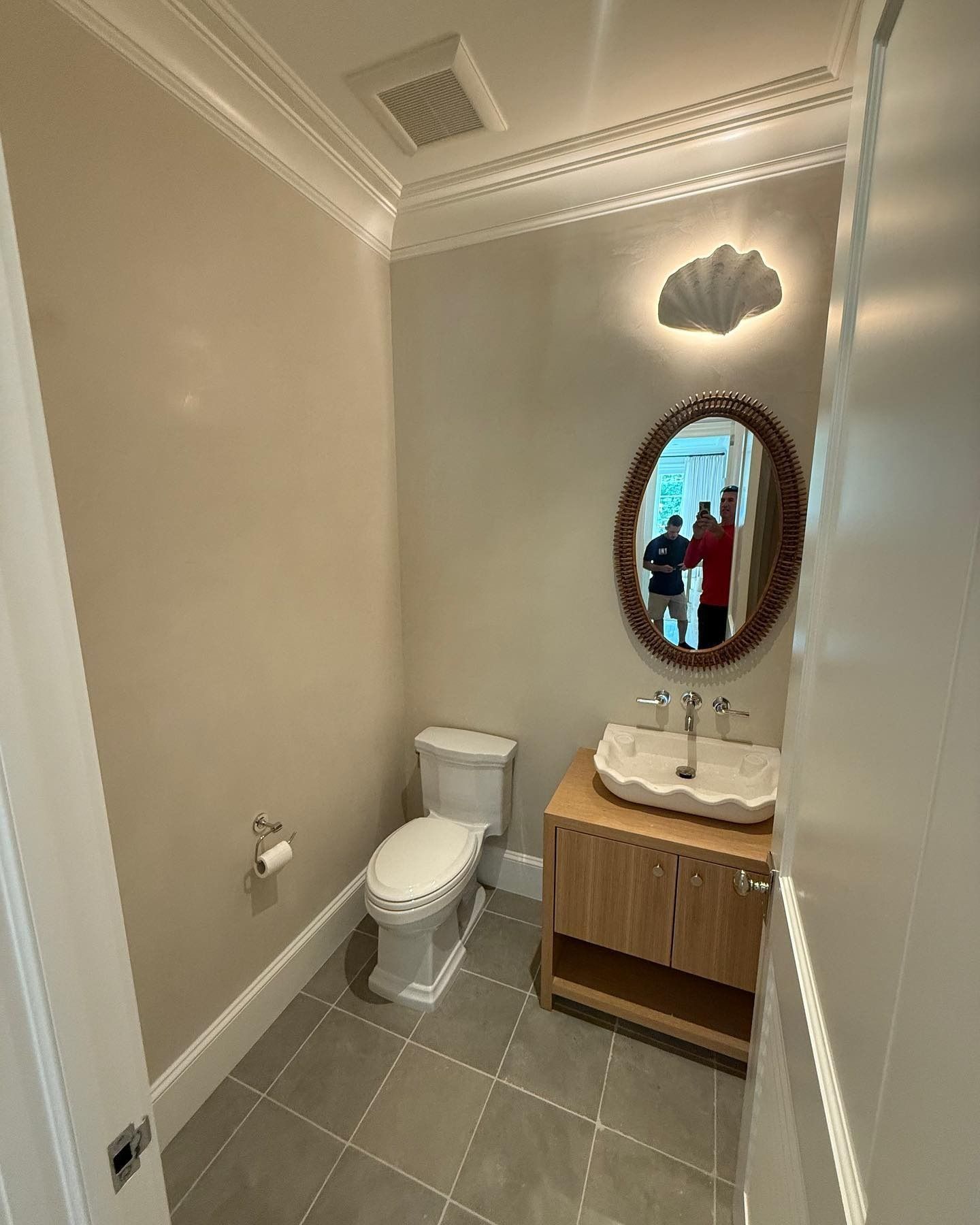 A small, light-colored bathroom with a toilet, vanity, and oval mirror.