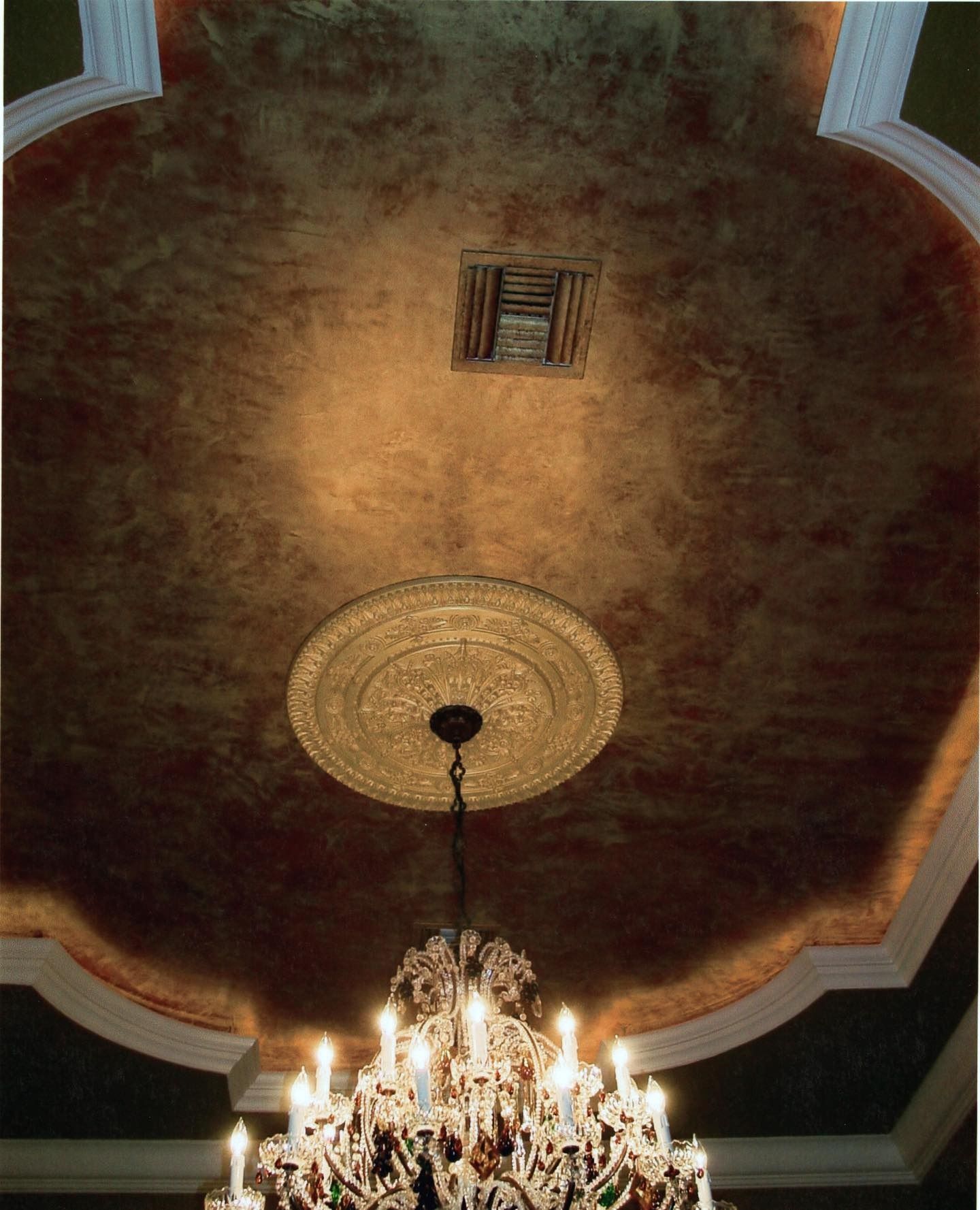 Ornate chandelier hanging from a gold-painted ceiling with a decorative molding.