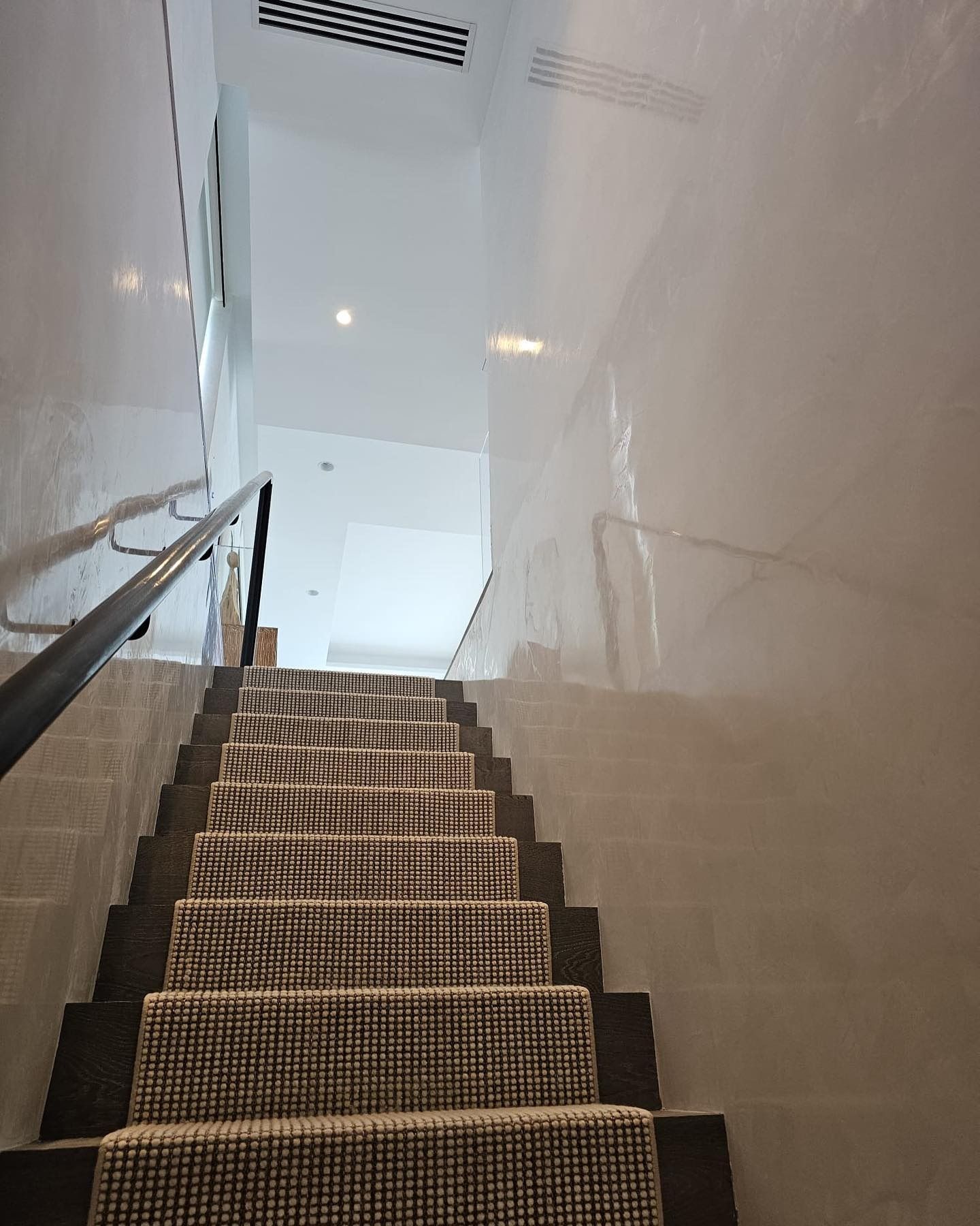 Staircase with checkered carpet runner, ascending to a bright hallway, with handrails on each side.