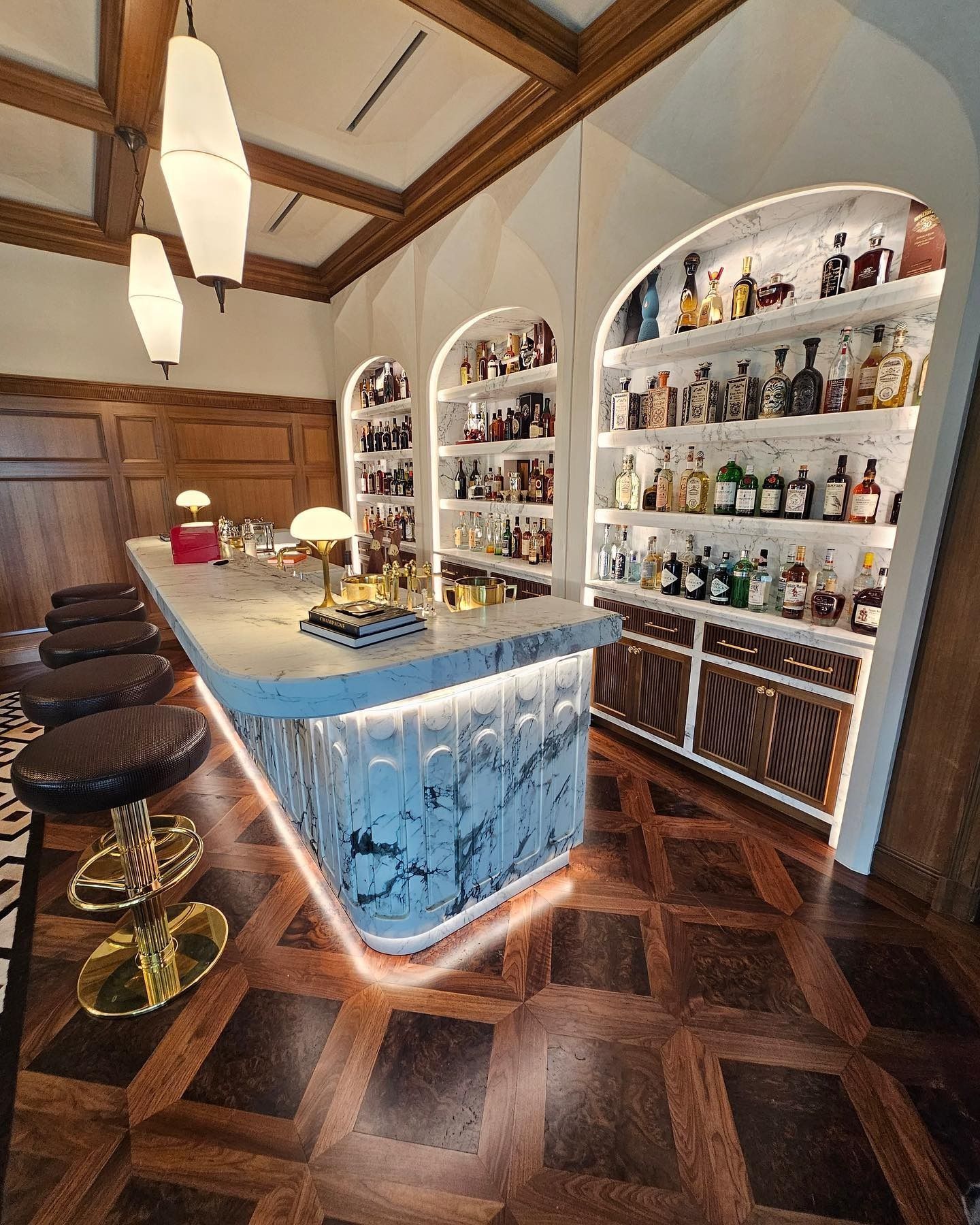 Upscale bar with marble countertop, wooden floors, and arched shelves filled with bottles.