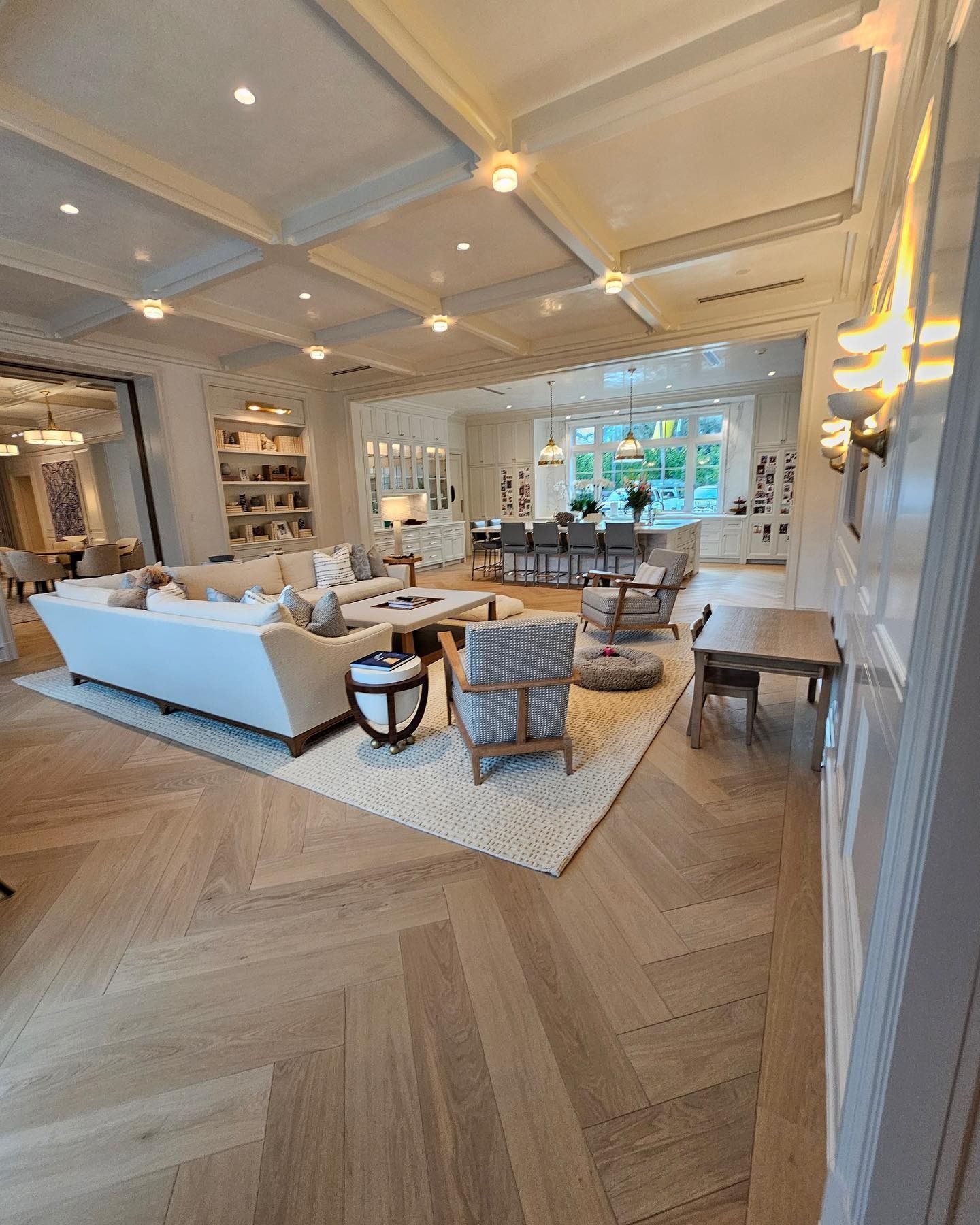 Spacious, light-filled living area with herringbone floors, white furniture, and built-in shelving.