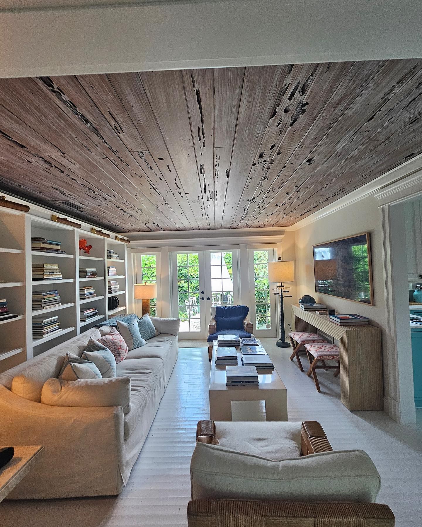 Living room with whitewashed floors, distressed wood ceiling, white built-in shelves, and a long white sofa.