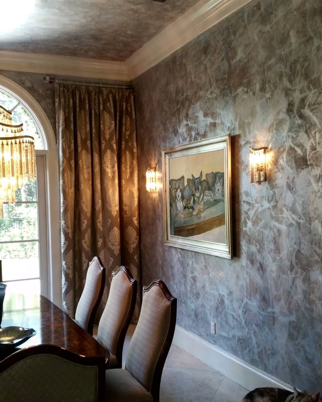 Dining room with textured gray walls, artwork, gold curtains, and chairs.