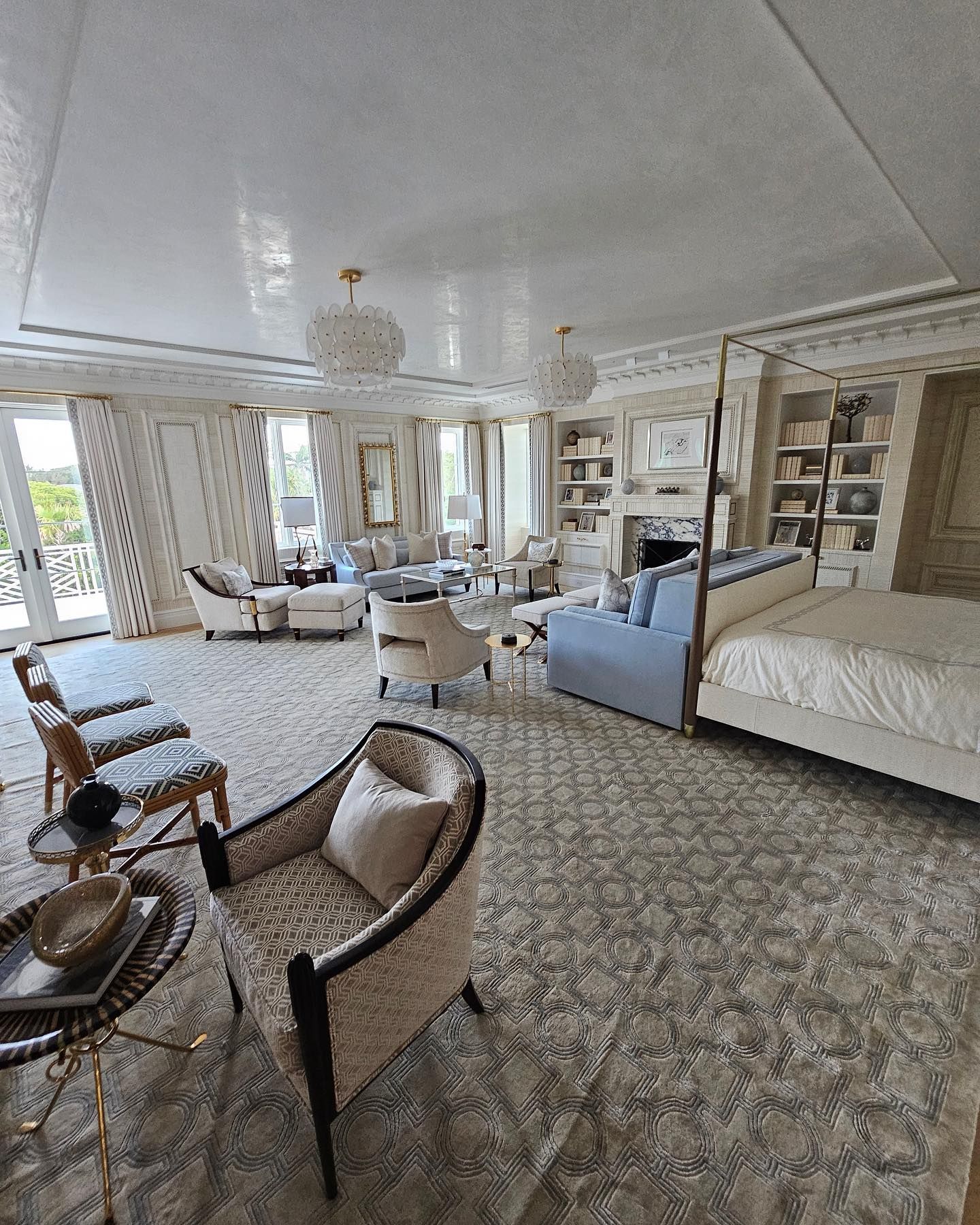 Spacious, luxurious bedroom with light colors, multiple seating areas, large windows, and a four-poster bed.