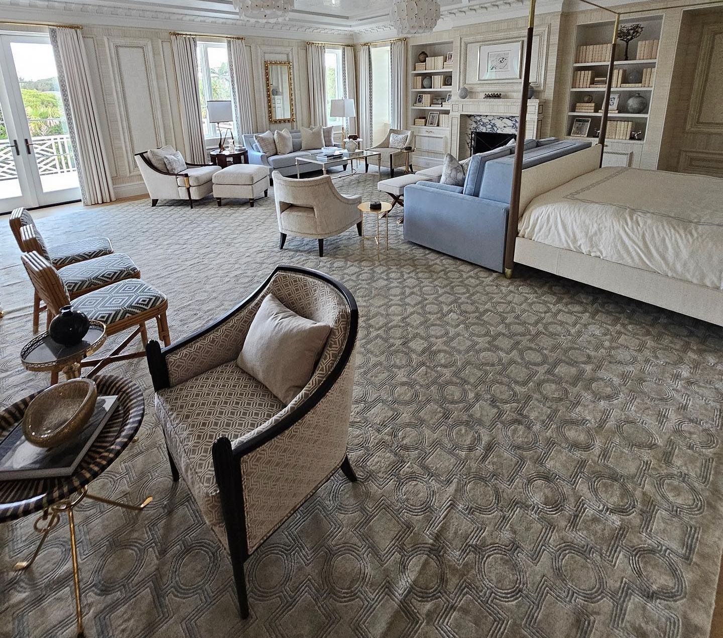 Spacious bedroom with light-colored furniture, patterned rug, and large windows overlooking trees.
