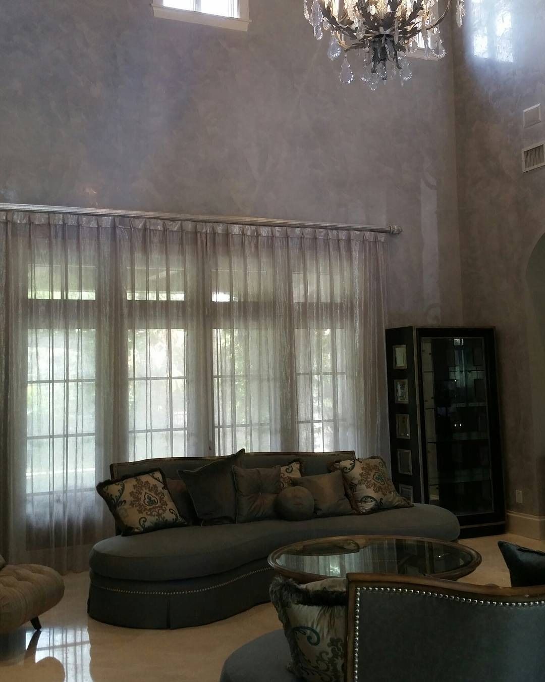 Living room with high ceiling, sheer curtains, gray curved sofa, and chandelier.